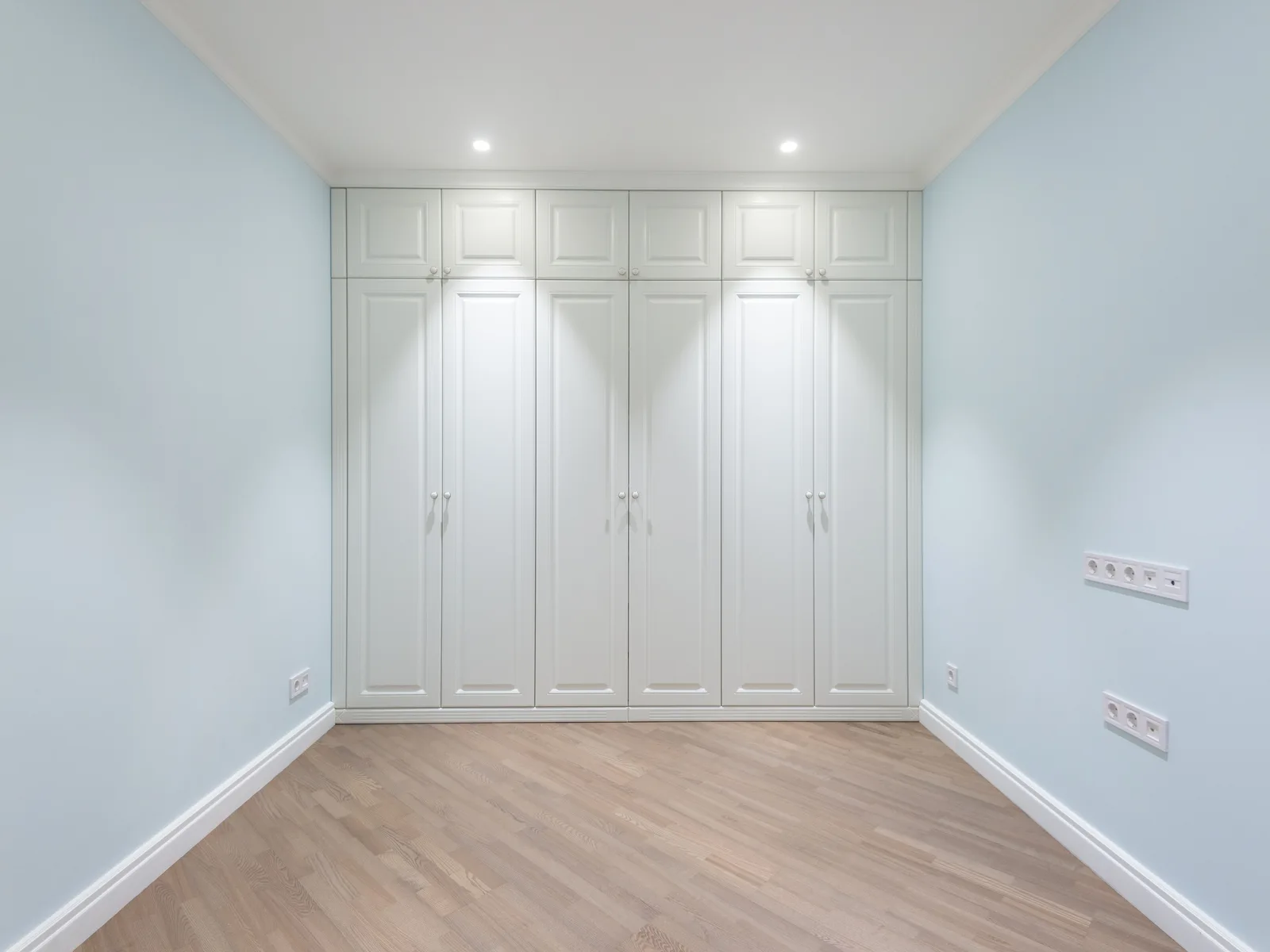 A floor-to-ceiling built-in wardrobe in sprayed painted MDF, six panelled doors closed, scribed to the ceiling and skirting of a finished room